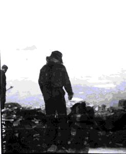 Image of Inuit man and 2 white men at shore; one holding a tool
