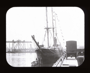 Image of Busy waterfront, vessel docked, truck on dock, large structure beyond