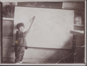 Image of Young boy at wall map, using pointer