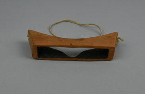 Image of Carved wooden goggles with large rectangular eye slit; held on by one soft thong