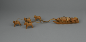 Image: carved wooden dog sled carrying small boat for dogs; 4 dogs in leather harnesses