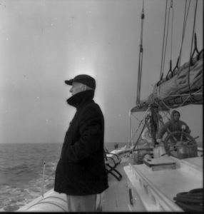 Image of Donald MacMillan on deck in Gulf of St. Lawrence. Crewman at wheel, beyond