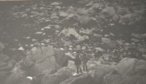 Image of 2 Eskimos [Inuit] and dog on rocky slope