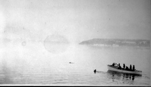Image of Eskimos [Inuit] in an open boat; one with rifle? Float near