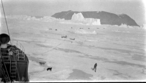 Image of Teams scattered on ice near ship; iceberg beyond