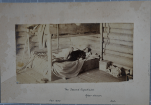 Image of Interior of a log cabin with man in bunkbed with caption The Second Expedition,