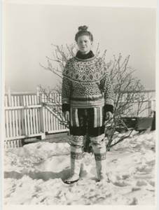 Image of Miriam MacMillan in her yard wearing Eskimo [Inuit] outfit. Hair in topknot
