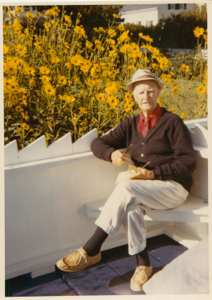 Image of Donald MacMillan sitting on his terrace by yellow daisies
