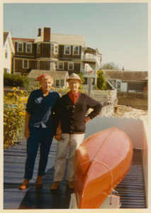 Image of Miriam and Donald MacMillan standing on their terrace overturned canoe