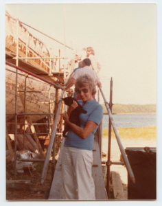 Image: Woman holding black cat; Schooner Bowdoin under reconstruction in background