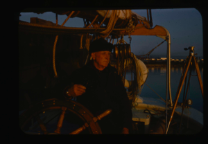 Image of Donald MacMillan at wheel.  (sunset colors)