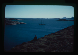 Image of Miriam MacMillan sitting on land overlooking harbor; icebergs in distance