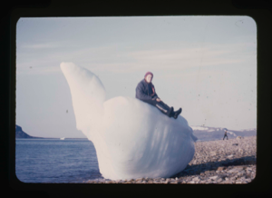Image of Miriam MacMillan sitting on odd-shaped, beached iceberg. (3 copies)