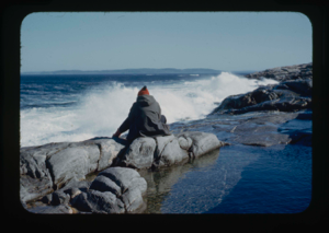 Image of Miriam MacMillan sitting on rocks watching surf (2 copies).