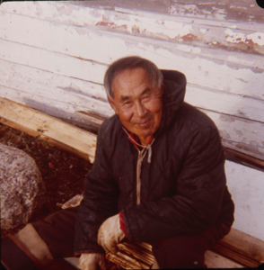 Image of Eskimo [Inuk] man sitting by boat