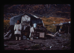 Image of Eskimo [Inuk] woman in front of her home.
