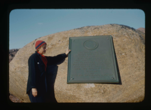 Image of Miriam MacMillan at Greely memorial, pointing to plaque