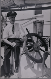 Image of Donald B. MacMillan next to wheel on board Bowdoin