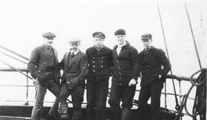 Image of Five men against ship rail. Donald MacMillan seated second from right