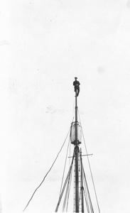 Image of Donald MacMillan sitting atop mast