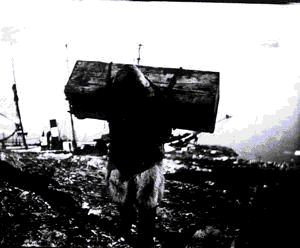 Image: Inuit man carrying wooden crate from ship on his back