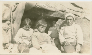 Image of Inuit family by stone house entrance