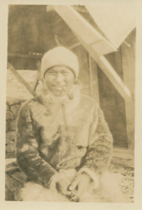 Image of Inuit man by stone/wood house entrance