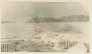 Image of The Bowdoin in ice. Crates and tents on shore