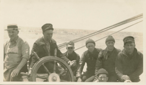 Image of Crew members by wheel. L>R: William Lewis, Richard Goddard, John Jaynes, Don Mix?, Donald MacMillan, ? and Ralph Robinson, seated