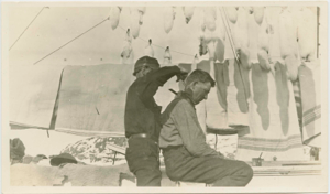 Image: Ralph Robinson getting a haircut on deck. Fox skins hanging