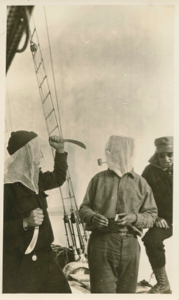 Image of Crew man in headnet with knives, ? in headnet with corncob pipe, and Thomas McCue