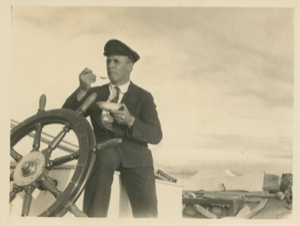 Image of Donald MacMillan by wheel, eating, perhaps, the last ice cream.