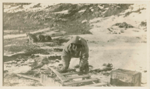 Image: Inuit man repairing sledge