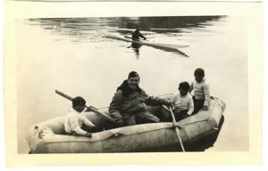 Image of Three Greenlandic boys and serviceman in rubber raft. Kayaker beyond