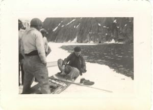 Image of Serviceman getting into kayak on snow, shoes on snow, Greenlandic men watching