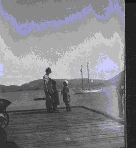 Image of Man and two children on pier. The BOWDOIN moored beyond