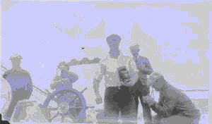 Image of Five men at wheel. One holds camera
