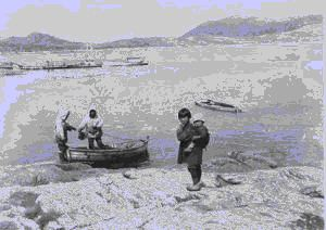 Image: Eskimos [Inuit] at water's edge; two men working in boat; girl carries child