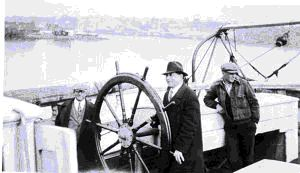 Image of Jack Crowell in overcoat and fedora, at wheel (Not the BOWDOIN.) Two men near
