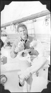 Image of Seated crewman holding two stuffed seal pups