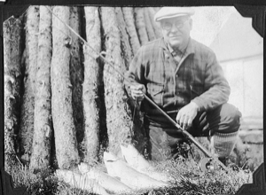 Image: ? with pole and four fish, by wood stack