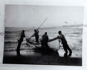 Image of Four men launching open boat . Vessel moored in distance 
