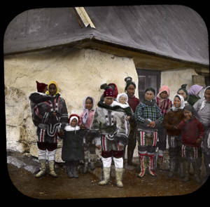 Image of West Greenland women and children at corner store. Danish children in hoods