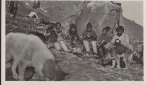Image of Inuit families by tupik, dogs near. Tent and supplies beyond