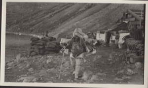 Image of Inuit woman by Borup Lodge, with roll of furs on her back
