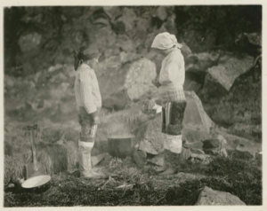 Image: Maligiak. Two Eskimo [Inuit] women standing beside a fire where they are boiling some fish (halibut).