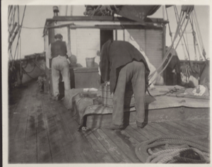 Image of Rear view of Captain Comer washing and the cook beside the galley door.