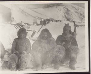 Image of Tong-we, Accomoding-wah and Ahng-o-de-blah-o [Three Inuit men sittiing on sledge. One has pipe. Ice saw and other tools beyond]