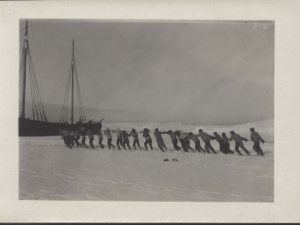 Image: Many men and women pulling rope toward moored vessel