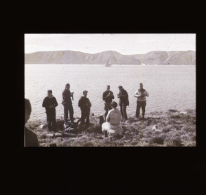 Image of Six crewmen photographing an Inuit man, sitting